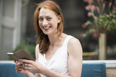 Portrait of happy redheaded woman with smartphone at sidewalk cafe - TAMF00774