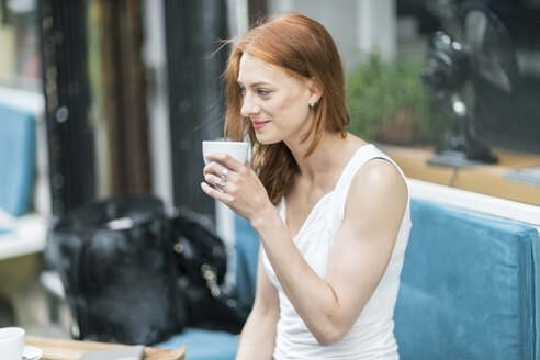 Rothaarige Frau trinkt Kaffee in einem Straßencafé - TAMF00776