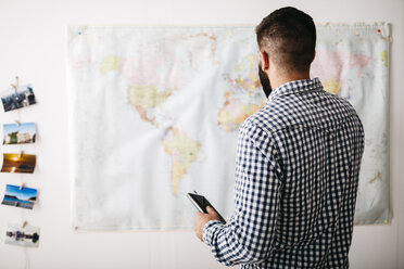 Young man selecting travel destinations on a world map - JRFF01036