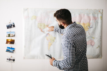 Junger Mann wählt Reiseziele auf einer Weltkarte aus - JRFF01037
