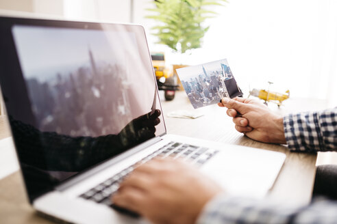 Junger Mann, der seine nächste Reise plant, mit Laptop und Foto in der Hand - JRFF01039