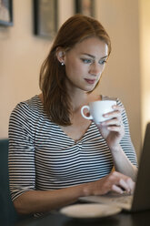 Portrait of woman sitting in a coffee shop using laptop - TAMF00785