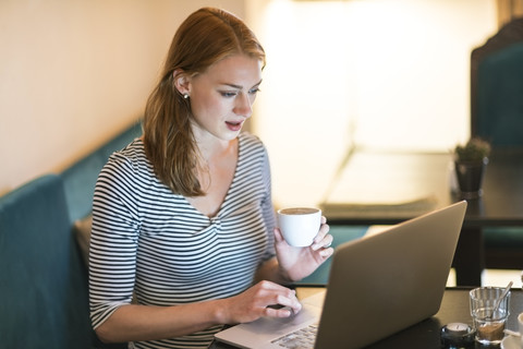 Porträt einer Frau, die in einem Café sitzt und einen Laptop benutzt, lizenzfreies Stockfoto