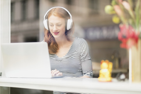 Lächelnde Frau, die in einem Café sitzt und Kopfhörer und Laptop benutzt, lizenzfreies Stockfoto