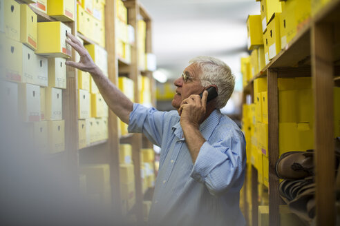 Senior man on the phone in warehouse with shoe boxes - ZEF11615