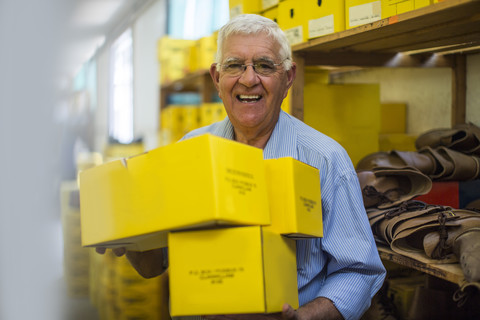 Smiling senior man in warehouse carrying shoe boxes stock photo
