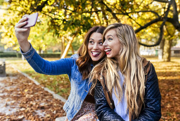 Zwei verspielte junge Frauen machen ein Selfie in einem Park im Herbst - MGOF02594