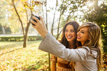 Two smiling young women taking a selfie in a park in autumn - MGOF02598