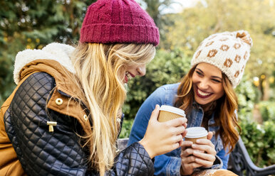 Zwei glückliche junge Frauen trinken Kaffee in einem Park im Herbst - MGOF02614