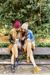 Zwei junge Frauen mit Smartphone in einem Park im Herbst - MGOF02615