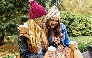Zwei junge Frauen mit Smartphone in einem Park im Herbst - MGOF02616