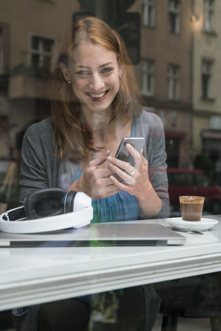 Porträt einer lächelnden Frau mit Smartphone in einem Kaffeehaus, lizenzfreies Stockfoto