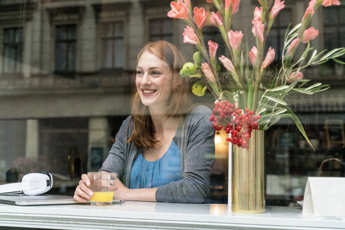 Porträt einer glücklichen Frau, die in einem Café sitzt und durch das Fenster schaut - TAMF00810