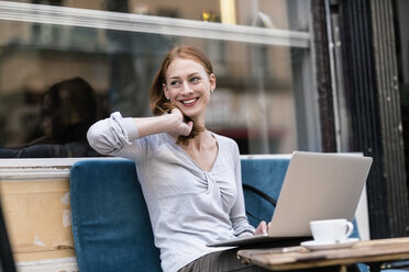 Lächelnde rothaarige Frau mit Laptop in einem Straßencafé - TAMF00814