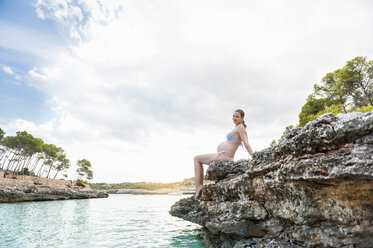 Pregnant woman sitting on rock at the sea - DIGF01425