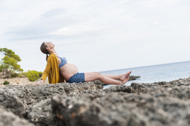 Pregnant woman sitting on rock at the sea - DIGF01446