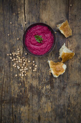 Schale mit Rote-Bete-Hummus, Kichererbsen und Fladenbrot auf dunklem Holz - LVF05581