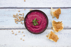 Bowl of beetroot hummus, chick-peas and flat bread on wood - LVF05585