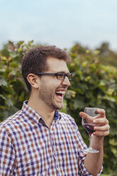 Glücklicher junger Mann in einem Weinberg mit einem Glas Rotwein in der Hand - ZEDF00427