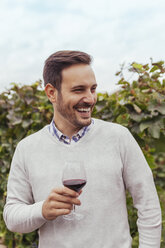 Glücklicher junger Mann in einem Weinberg mit einem Glas Rotwein in der Hand - ZEDF00428