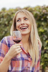 Happy young woman in a vineyard holding glass of red wine - ZEDF00429