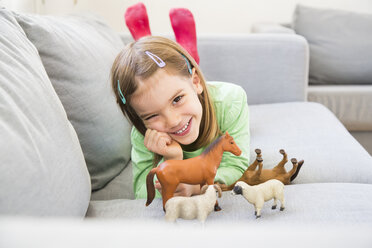 Porträt eines lächelnden kleinen Mädchens auf der Couch mit ihren Tierfiguren - LVF05594