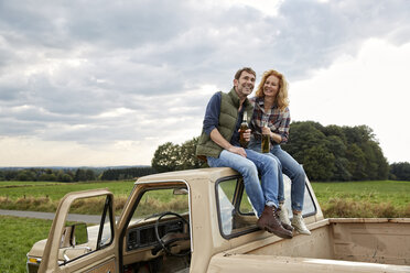 Couple sitting on pick up truck having a beer - FMKF03215