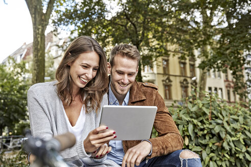 Lächelndes junges Paar benutzt Tablet im Park - FMKF03228