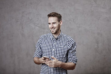 Lächelnder junger Mann mit Mobiltelefon in der Hand - FMKF03244