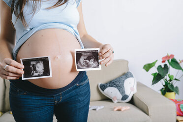 Schwangere Frau hält Ultraschallbilder vor ihren Bauch - GEMF01245