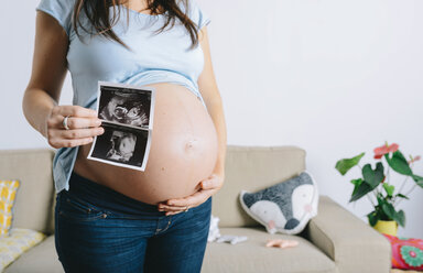 Schwangere Frau hält Ultraschallbilder vor ihren Bauch - GEMF01246