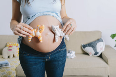 Pregnant woman holding soft toys in front of belly - GEMF01247