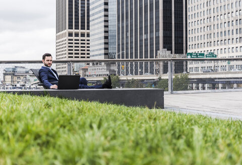 USA, New York, Manager in Manhattan sitting outdoor, using laptop - UUF09200