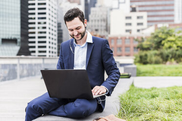 USA, New York, Manager in Manhattan sitting outdoor, using laptop and earphones - UUF09208