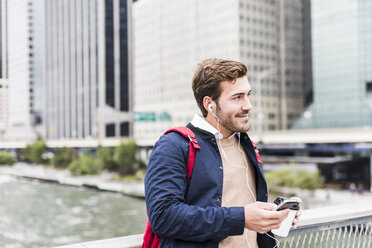 USA, New York, Businessan in Manhattan using smart phone and earphones - UUF09211