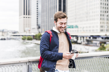 USA, New York, Geschäftsmann in Manhattan mit Smartphone und Kopfhörern - UUF09212