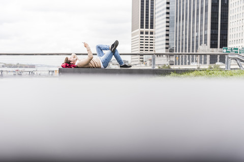 USA, New York, Geschäftsmann in Manhattan mit Smartphone, auf dem Rücken liegend, lizenzfreies Stockfoto