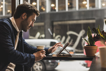 USA, New York City, Geschäftsmann sitzt in einem Café und benutzt ein digitales Tablet - UUF09231