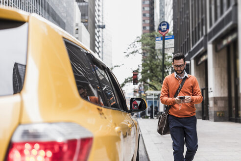 USA, New York City, Geschäftsmann nähert sich einem Taxi und benutzt ein Smartphone - UUF09244