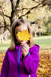 Little girl hiding her face behind an autumn leaf - LVF05595