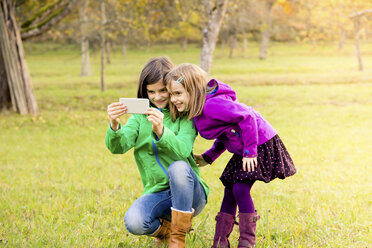 Zwei lächelnde Schwestern nehmen Selfie mit Handy auf einer Wiese im Herbst - LVF05599