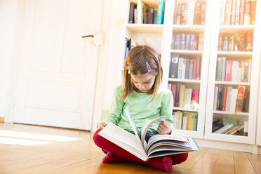 Kleines Mädchen sitzt auf dem Boden und beobachtet das Umblättern eines Buches - LVF05603