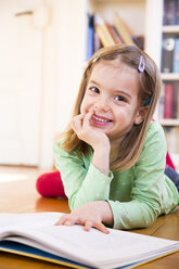 Porträt eines lächelnden kleinen Mädchens, das mit einem Buch auf dem Boden liegt - LVF05604