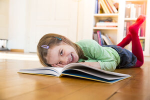 Lachendes kleines Mädchen mit einem Buch auf dem Boden liegend - LVF05605