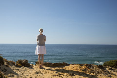 Frau steht an der Küste und schaut in die Ferne, lizenzfreies Stockfoto