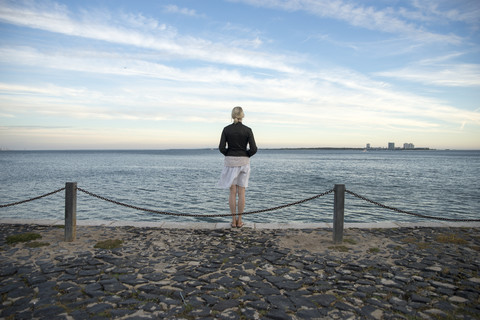 Portugal, Setubal, Frau steht am Meer und schaut auf die Halbinsel Troia, lizenzfreies Stockfoto