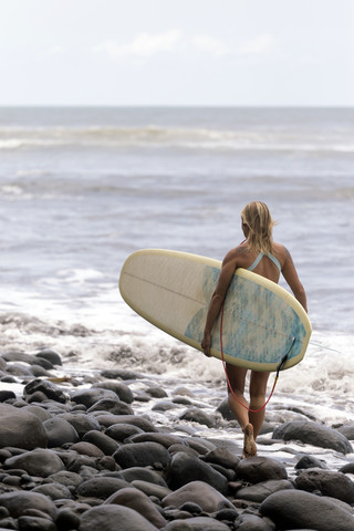 Indonesien, Bali, Frau mit Surfbrett auf dem Meer, lizenzfreies Stockfoto