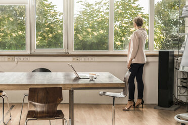 Geschäftsfrau steht am Fenster in einem modernen Konferenzraum - RIBF00591