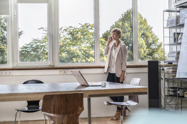 Businesswoman talking on cell phone in modern conference room - RIBF00592