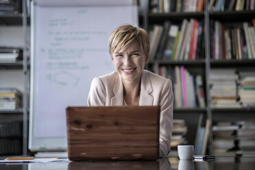 Portrait of smiling businesswoman with laptop in modern conference room - RIBF00598